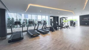 Un gimnasio moderno con cintas de correr, elípticas y equipo de levantamiento de pesas. Amplias ventanas ofrecen luz natural y vistas al exterior.