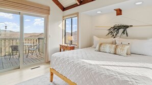 A bedroom with a large bed, a balcony with chairs, and a view of the hills. - “High Haven — A Modern Mountain Retreat with Breathtaking Views” (Sugar Mountain)