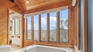 A wooden cabin with a large window, a bathtub, and a door leading to another room. - “High Haven — A Modern Mountain Retreat with Breathtaking Views” (Sugar Mountain)