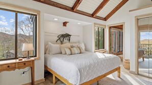 A bedroom with a large bed, wooden beams, a ceiling fan, and a view of the outdoors. - “High Haven — A Modern Mountain Retreat with Breathtaking Views” (Sugar Mountain)