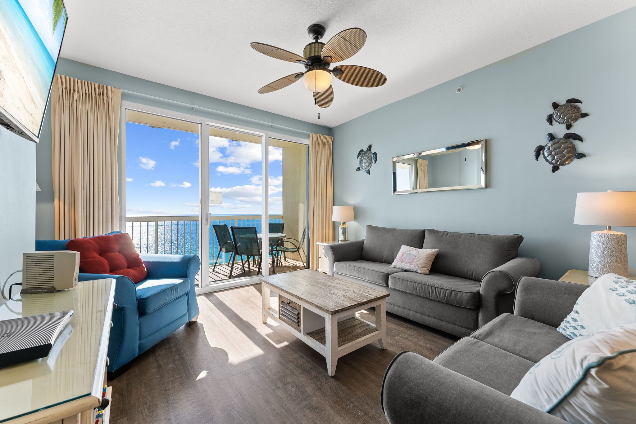 A living room with a large window, a ceiling fan, and a view of the ocean.