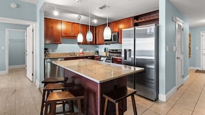 A modern kitchen with granite countertops, stainless steel appliances, wooden cabinets, and pendant lighting. - Waterfront condo w/ gulf views & resort pools (Panama City Beach)