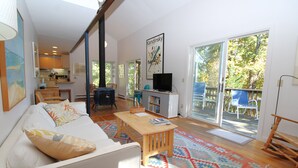 Een ruime woonkamer met een bank, een salontafel en een televisie. Een groot raam biedt uitzicht op het buitenland.