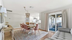 Una sala de estar moderna con un sofá gris, un comedor con sillas rosadas y una araña.
