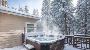 Een hottub op een houten terras, met besneeuwde bomen op de achtergrond.