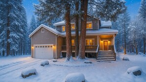 Een tweelaags huis met een overdekte veranda en een garage, omringd door met sneeuw bedekte bomen.
