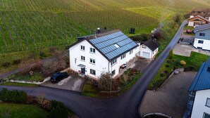A white two-story house with solar panels on the roof, a driveway, and a road in the foreground. - Apartment 'Wiedergrün' with Balcony and Wi-Fi (Durbach)