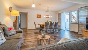 A modern living room with a sofa, a coffee table, a dining area with chairs, and a kitchen visible through an open door. - Apartment 'Wiedergrün' with Balcony and Wi-Fi (Durbach)