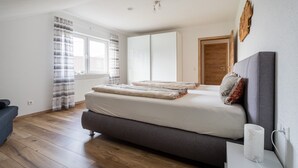 A bedroom with a bed, a bedside table, a lamp, a window with curtains, and a door. - Apartment 'Wiedergrün' with Balcony and Wi-Fi (Durbach)