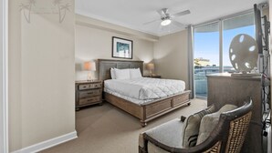 Ein Schlafzimmer mit Bett, Nachttischen, einem Sessel, einem Deckenventilator und einem großen Fenster mit Blick.