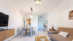 A modern living room with a sofa, coffee table, TV, and dining area. - SR Ground floor flat with direct access to the pool! (Marbella)