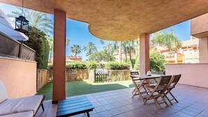 A covered patio with a table and chairs, a hanging lantern, and a view of a well-maintained lawn and buildings in the background. - SR Ground floor flat with direct access to the pool! (Marbella)
