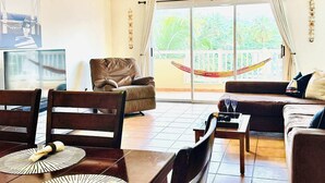 Ein geräumiger Wohnbereich mit Esstisch für zwei Personen, einer Couch und einer Hängematte neben der Glasschiebetür.
