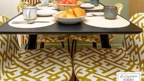 Een eetgedeelte met een gedekte tafel voor het ontbijt, inclusief croissants en fruit, en gestreept beklede stoelen.