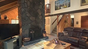 Een ruime woonkamer met een stenen openhaard, een grote bank en een televisie.