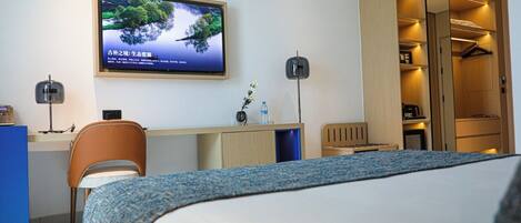A hotel room with a bed, a desk, a chair, a TV on the wall, and a wardrobe.
