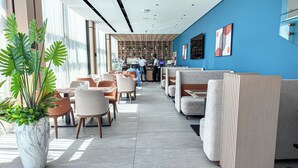 A modern hotel lobby with seating areas, a reception desk, and a large window providing natural light.