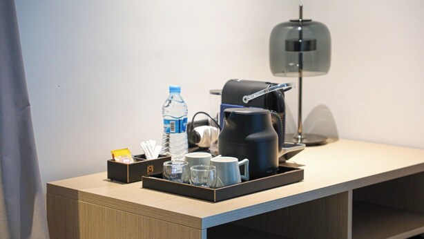 Une chambre d’hôtel avec un bureau en bois, une bouteille d’eau, une machine à café, des verres et un plateau avec une tasse et une petite boîte.
