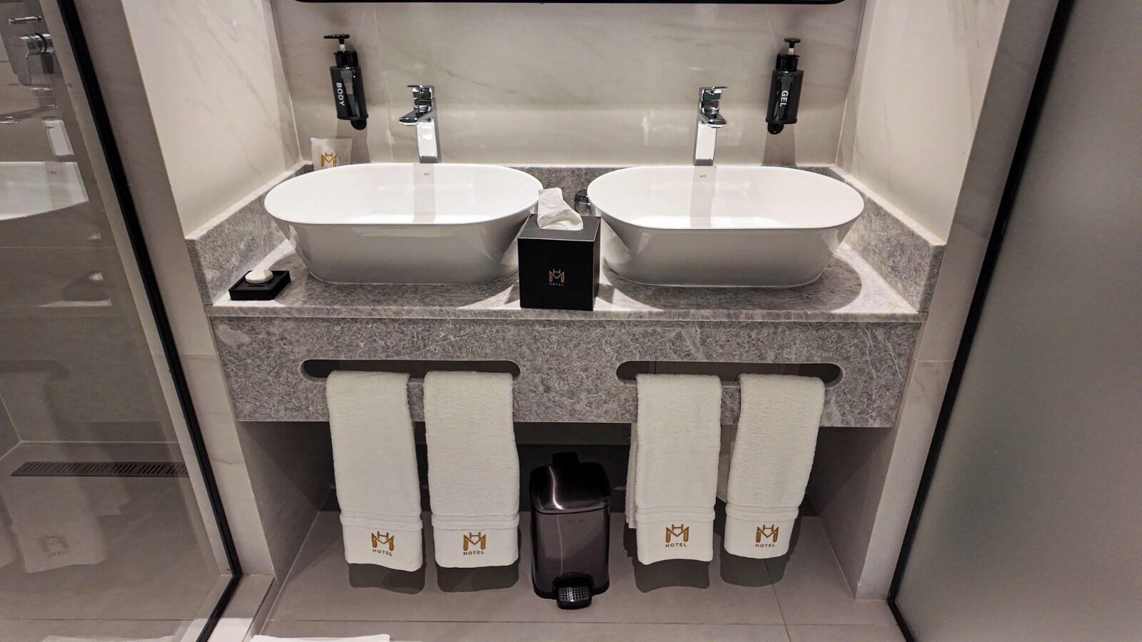 Une salle de bain avec deux lavabos, un porte-serviettes et une poubelle.