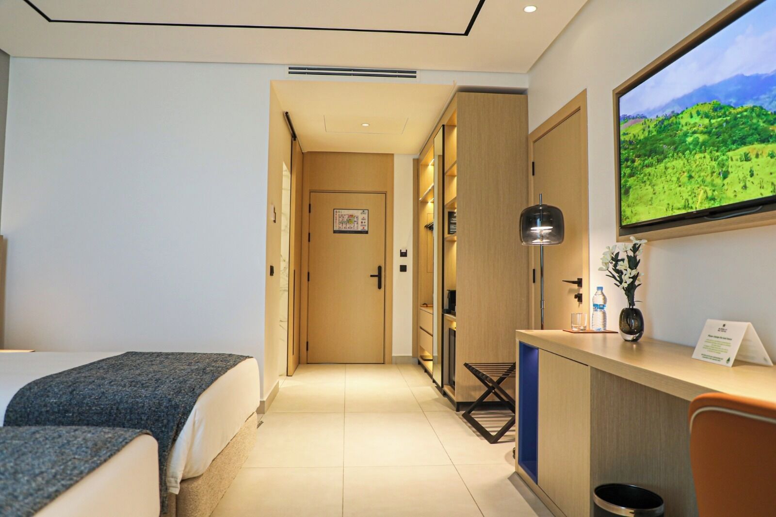 Habitación de hotel con cama, escritorio con ordenador, televisor y vistas a un paisaje verde.