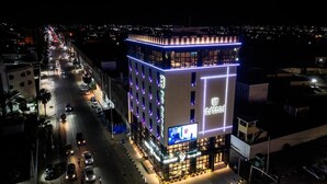A multi-story hotel with a prominent 'MH Hotel' sign, featuring a modern design with illuminated lines and a balcony on the upper floor.