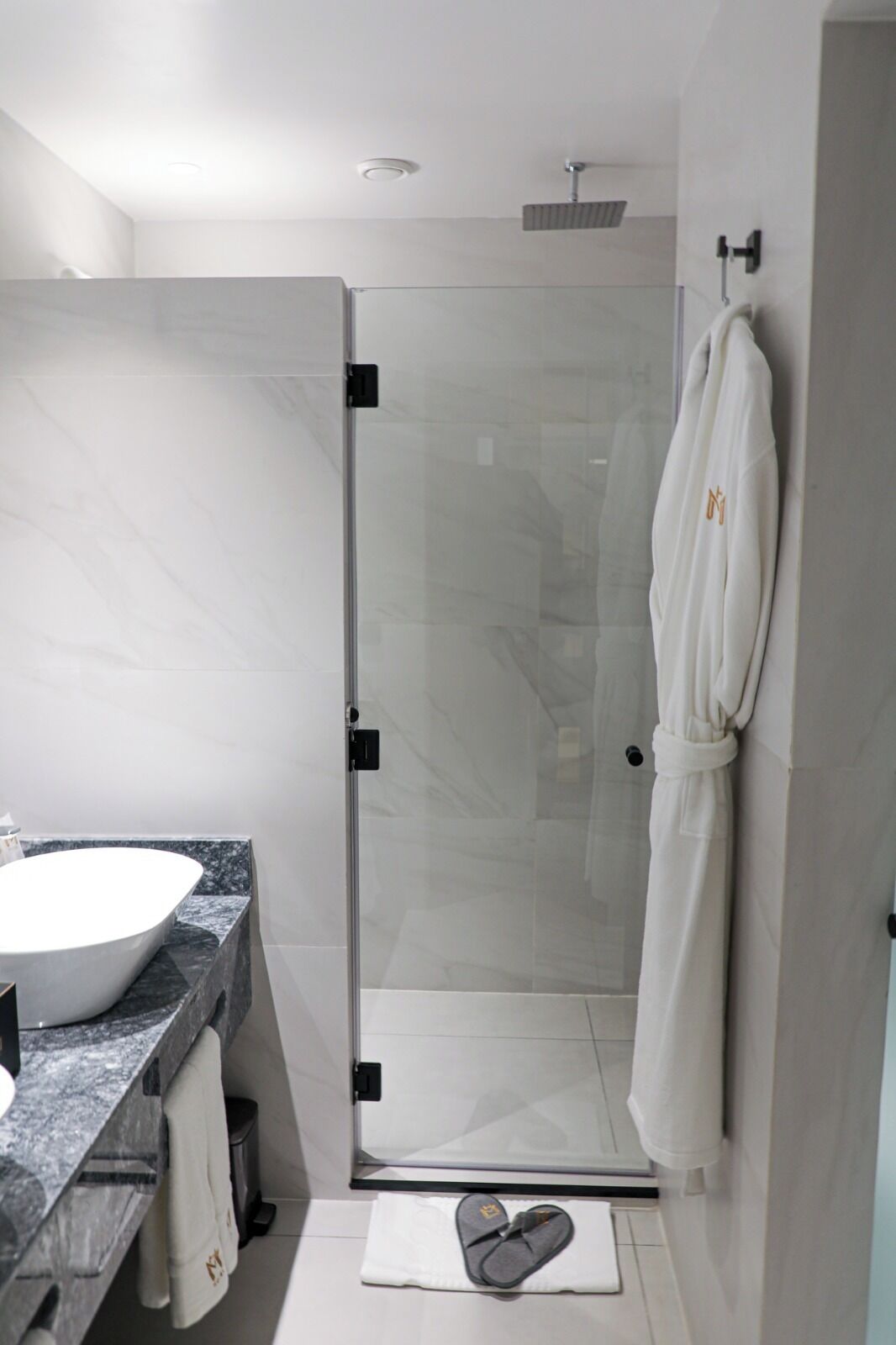 Een moderne badkamer met een douchecabine van glas, een marmeren wastafel en een badjas aan de muur.