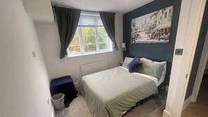 Ein Schlafzimmer mit einem Bett, einem Fenster mit Vorhängen, einem Heizkörper, einer Wandlampe und einem Gemälde.