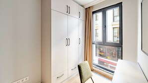 Een kamer met een grote garderobe, een stoel en een raam met uitzicht op gebouwen.