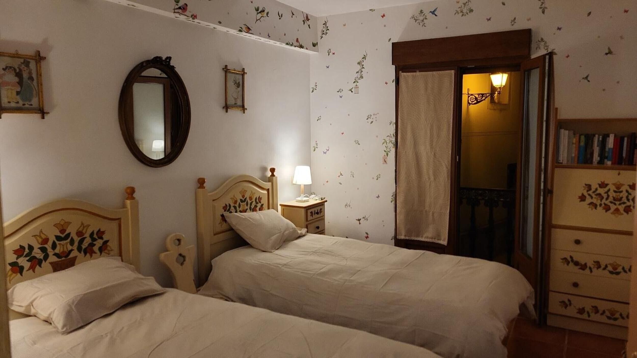 Ein Schlafzimmer mit zwei Betten, einem Spiegel, einem Nachttisch, einer Kommode und einer Tür, die auf einen Balkon führt.