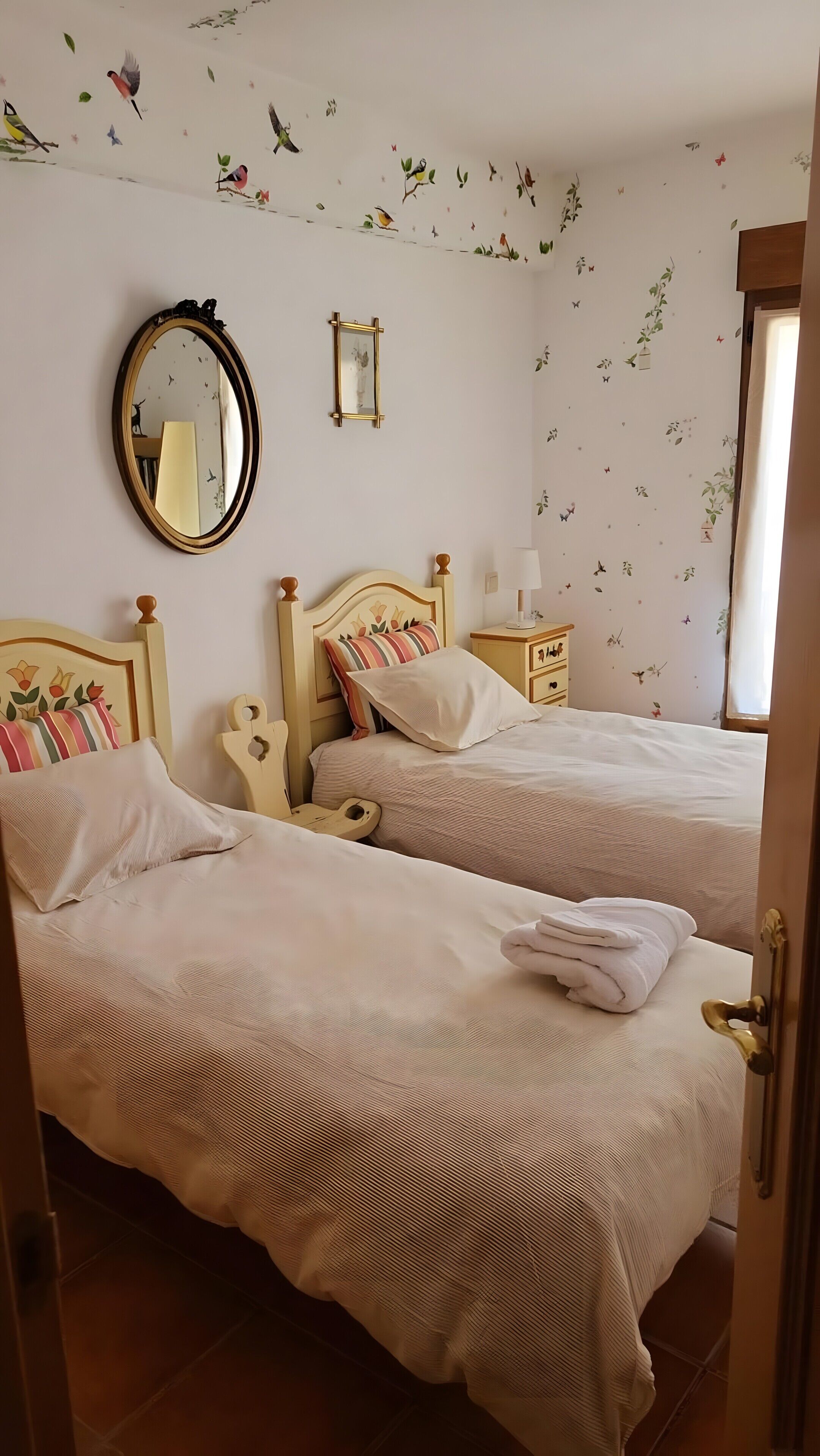 Una habitación con dos camas, un espejo, una mesita de noche y una ventana.