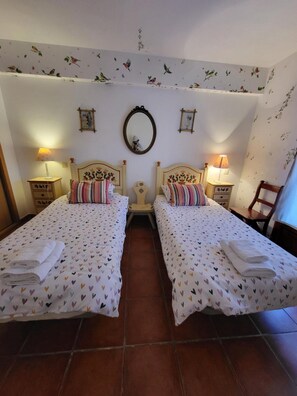 Ein Zimmer mit zwei Betten, jedes mit einer bettbezogenen Herzdecke, einem Spiegel an der Wand und einem floralen Wanddesign.