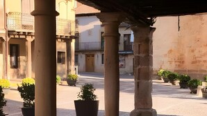 Une cour pavée de pierres, avec des colonnes en pierre, des plantes en pot et des bâtiments en arrière-plan.