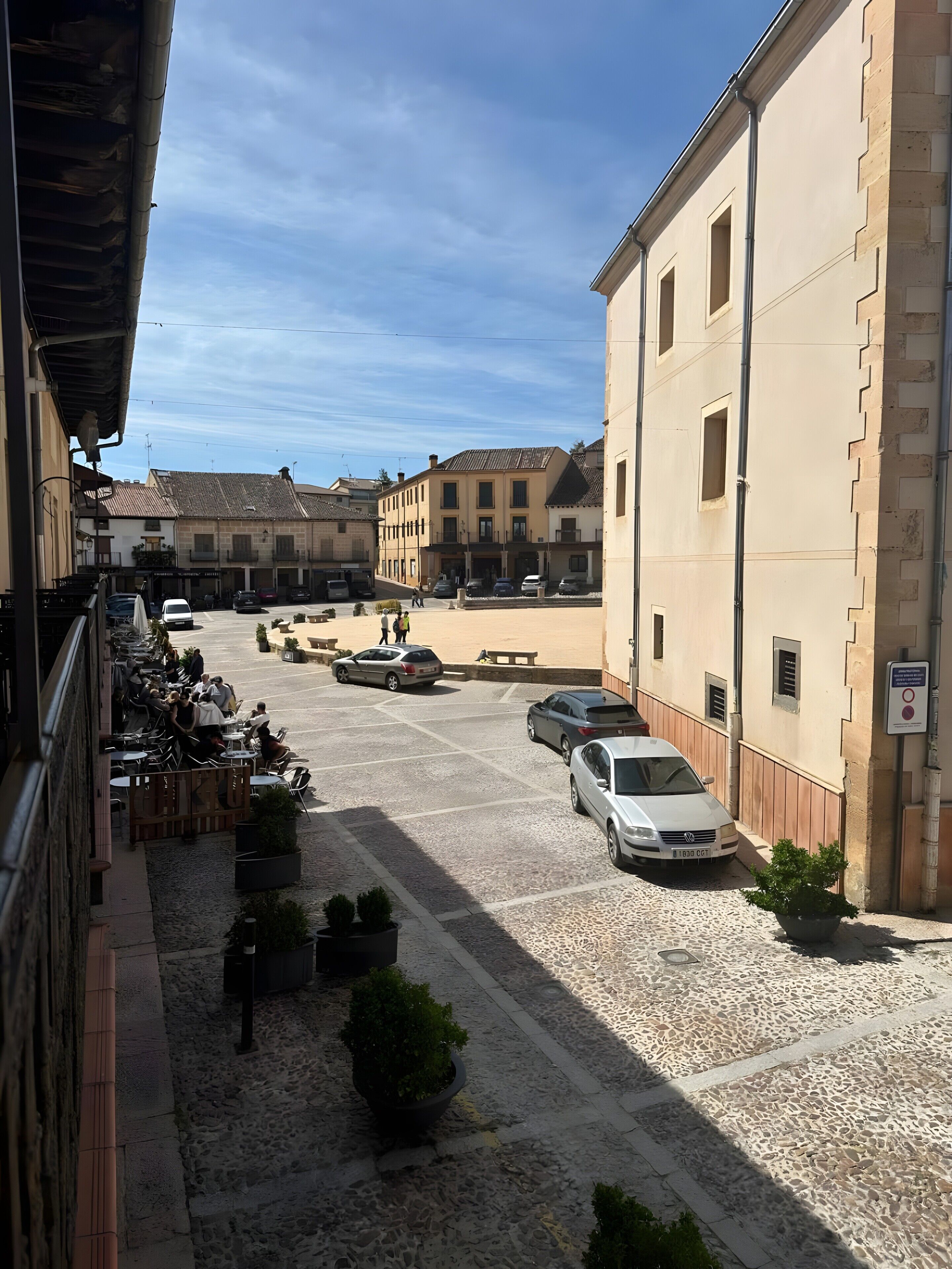 Un patio con mobiliario exterior, coches aparcados y edificios de arquitectura tradicional.
