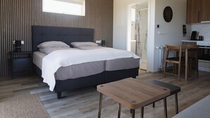 Ein Schlafzimmer mit einem großen Bett, Nachttischen, einer hölzernen Bank, einem Fenster und einer Küchenzeile mit Schränken und Geräten.