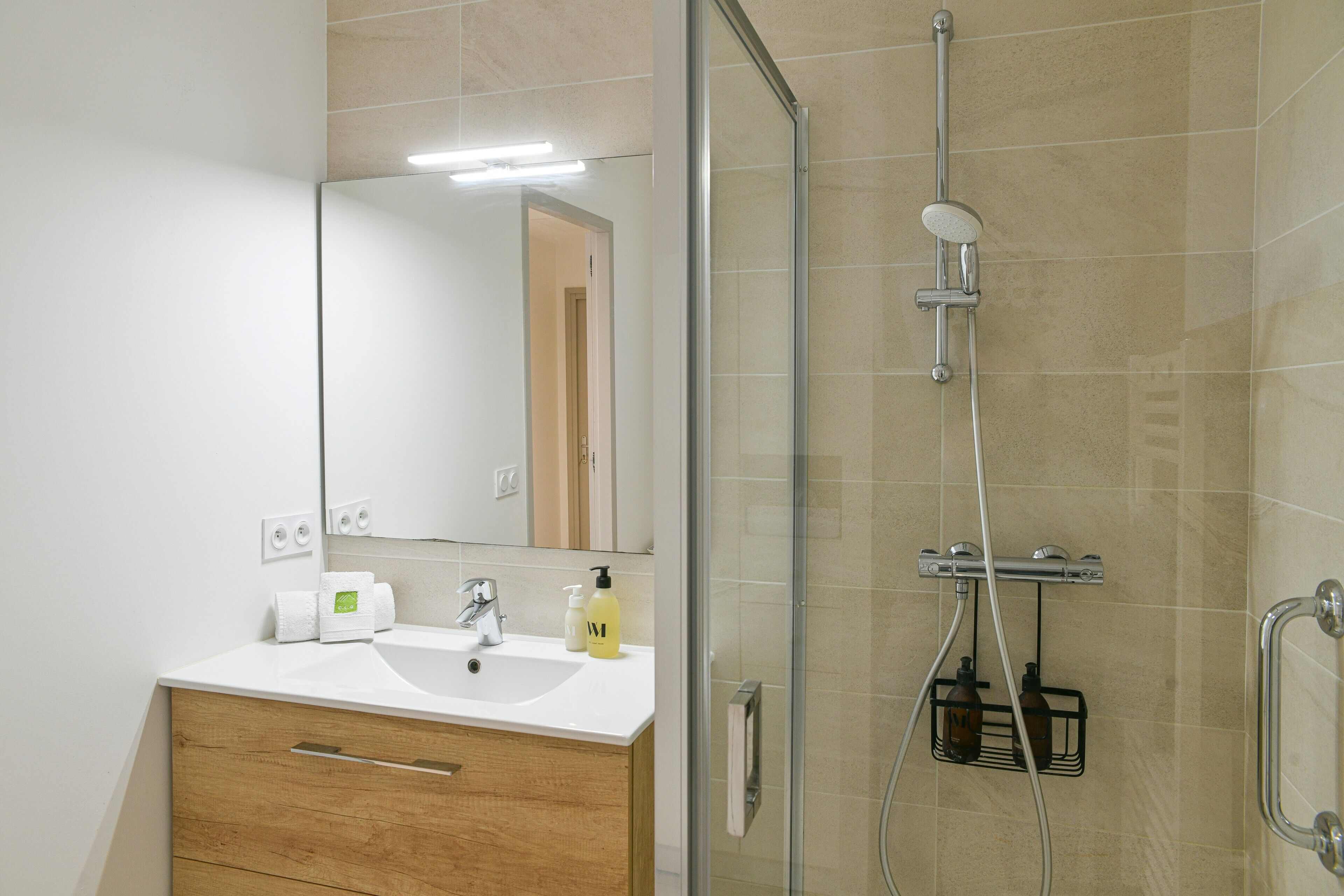 A bathroom with a glass shower enclosure, a sink with a mirror, and toiletries on the counter.