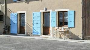 Un bâtiment avec des volets bleus, une petite table et des chaises à l’extérieur.