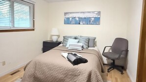 Een slaapkamer met een bed, nachtkastje, stoel en een schilderij aan de muur.