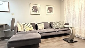 Een moderne woonkamer met een grijze modulaire bank, een glazen salontafel en twee kunstwerken met bloemmotieven aan de muur.