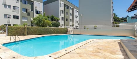 A swimming pool with tiled flooring, surrounded by apartment buildings.