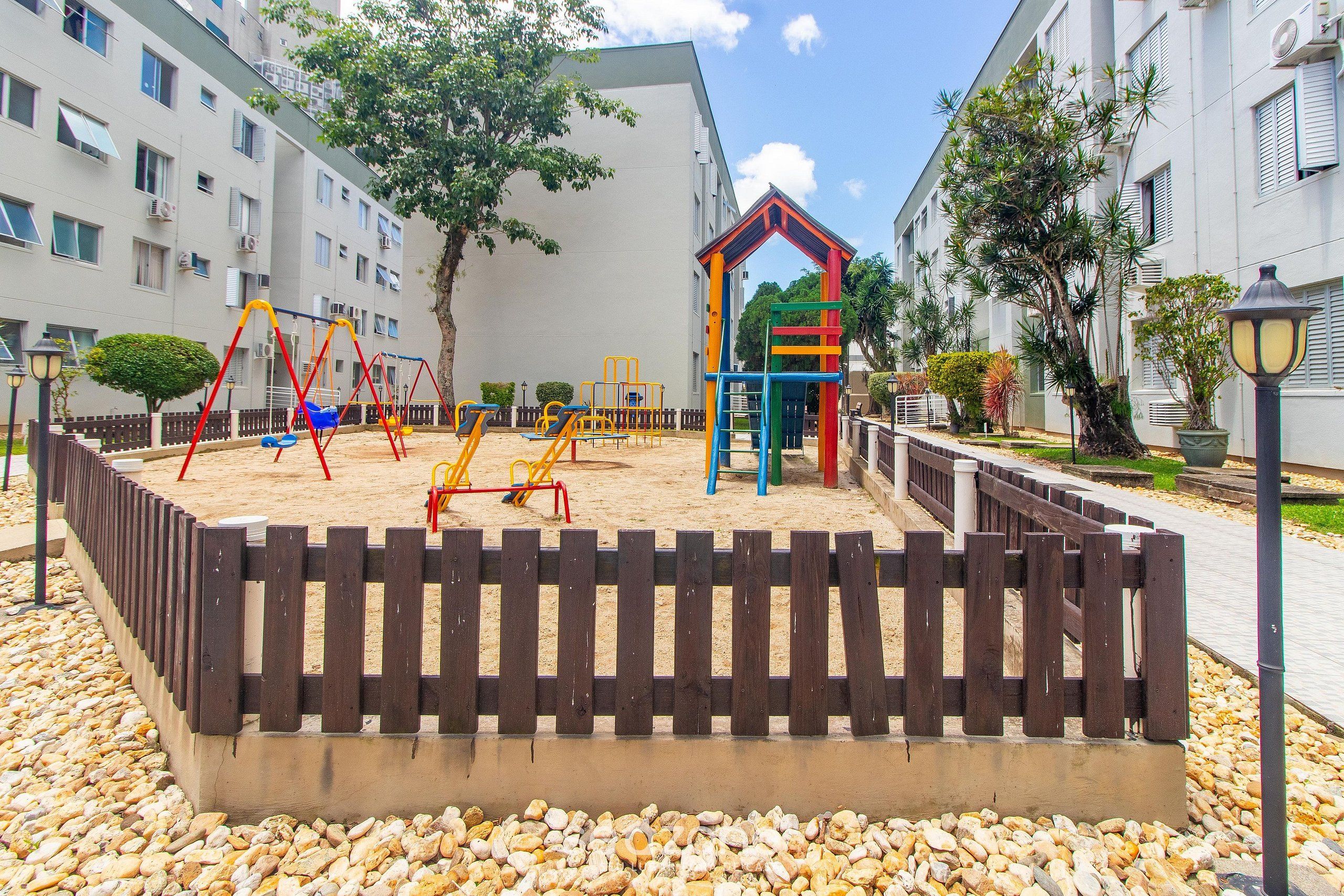 Un parque infantil con columpios y estructuras para escalar, rodeado por una valla de madera y piedras.