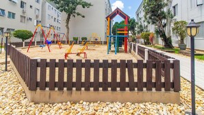 A playground with swings and climbing structures, surrounded by a wooden fence and pebbles. - Apt 650 m From Masc in Floripa Bas0401 (Florianópolis)