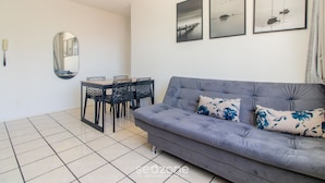 A living room with a grey sofa, two floral cushions, a dining table with chairs, and three framed pictures on the wall. - Apt 650 m From Masc in Floripa Bas0401 (Florianópolis)