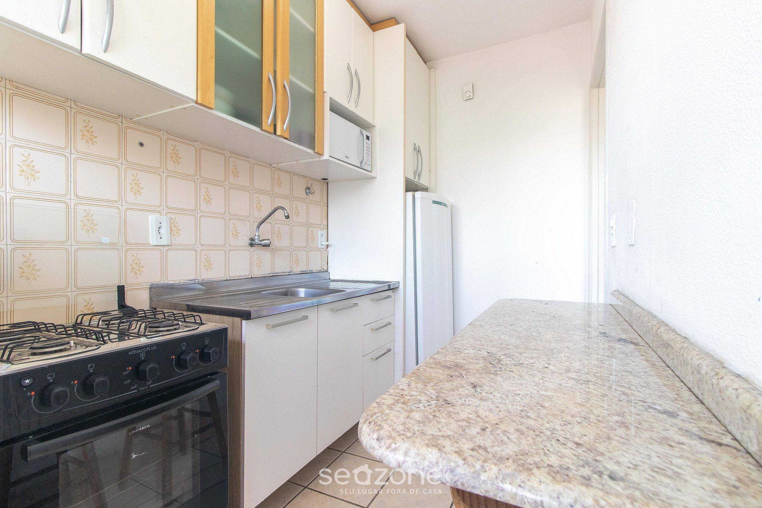 A kitchen with a gas stove, oven, stainless steel sink, and white cabinets.