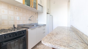 A kitchen with a gas stove, oven, stainless steel sink, and white cabinets. - Apt 650 m From Masc in Floripa Bas0401 (Florianópolis)