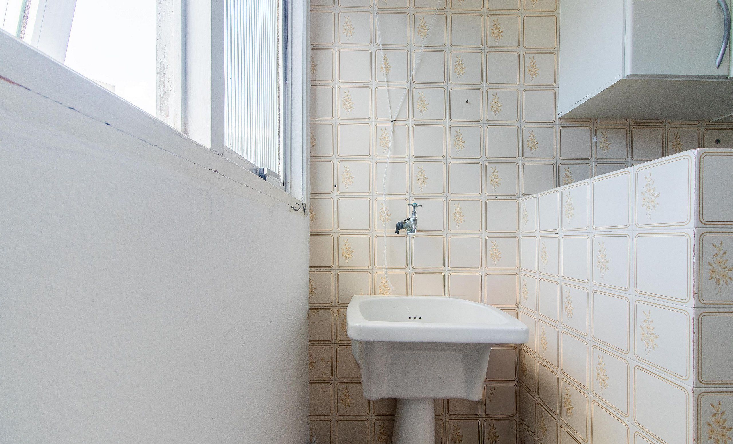 Casa de banho com lavatório, janela e azulejos estampados.