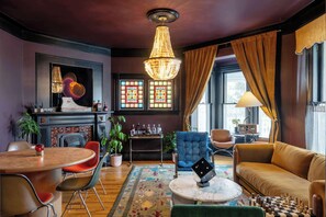 A room with a chandelier, a fireplace, a dining table, a sofa, and a chessboard.