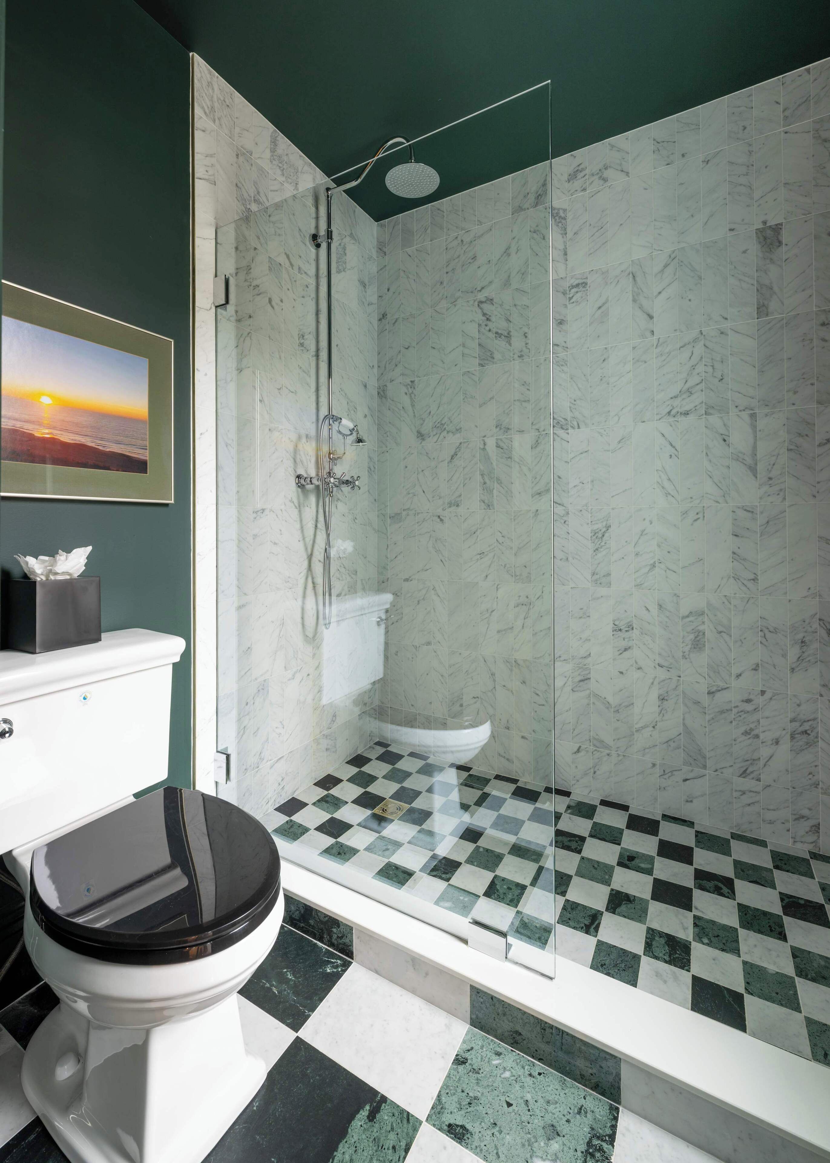 A bathroom with a checkered floor, a toilet, a shower with a glass door, and a framed picture on the wall.