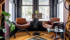 A room with two brown leather chairs, a glass table with a decorative item, a small table with a framed picture, and a large window with curtains. - The Turret - Ash Street Inn (Manchester)