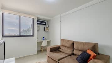 A modern living room with a brown sofa, a small white desk, and a large window.