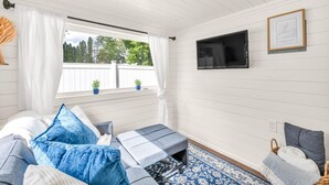 Ein gemütliches Zimmer mit einem Bett, einer kleinen Sitzecke, einem Fernseher und einem Fenster mit Blick auf Bäume.